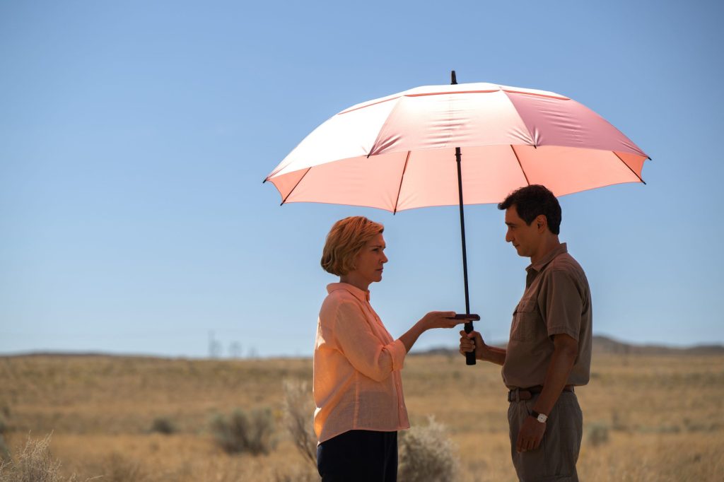 still from pluribus show featuring two characters facing one another under an umbrella